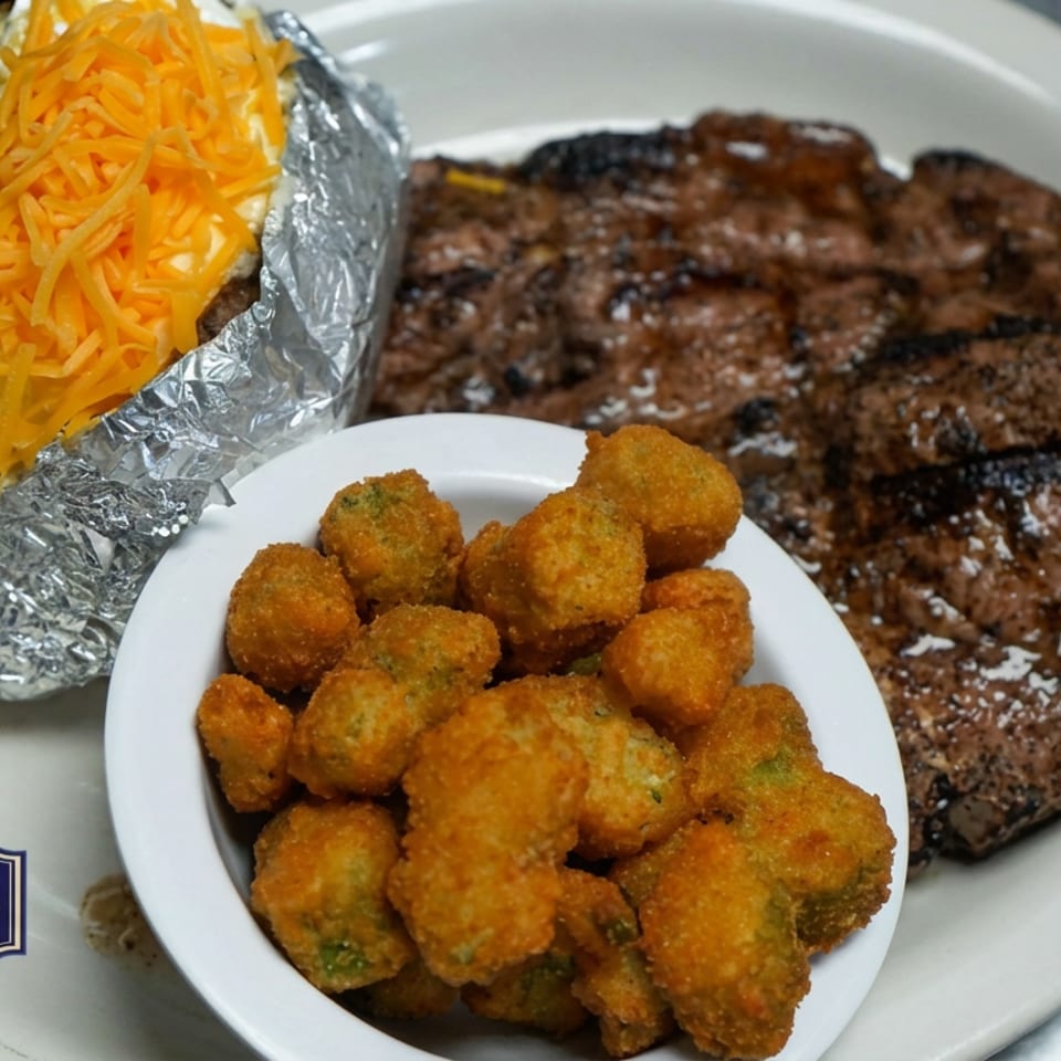 Grilled steak with a cheddar-topped baked potato and fried golden bites on a plate at Crosswoods Restaurant & Sports Club.